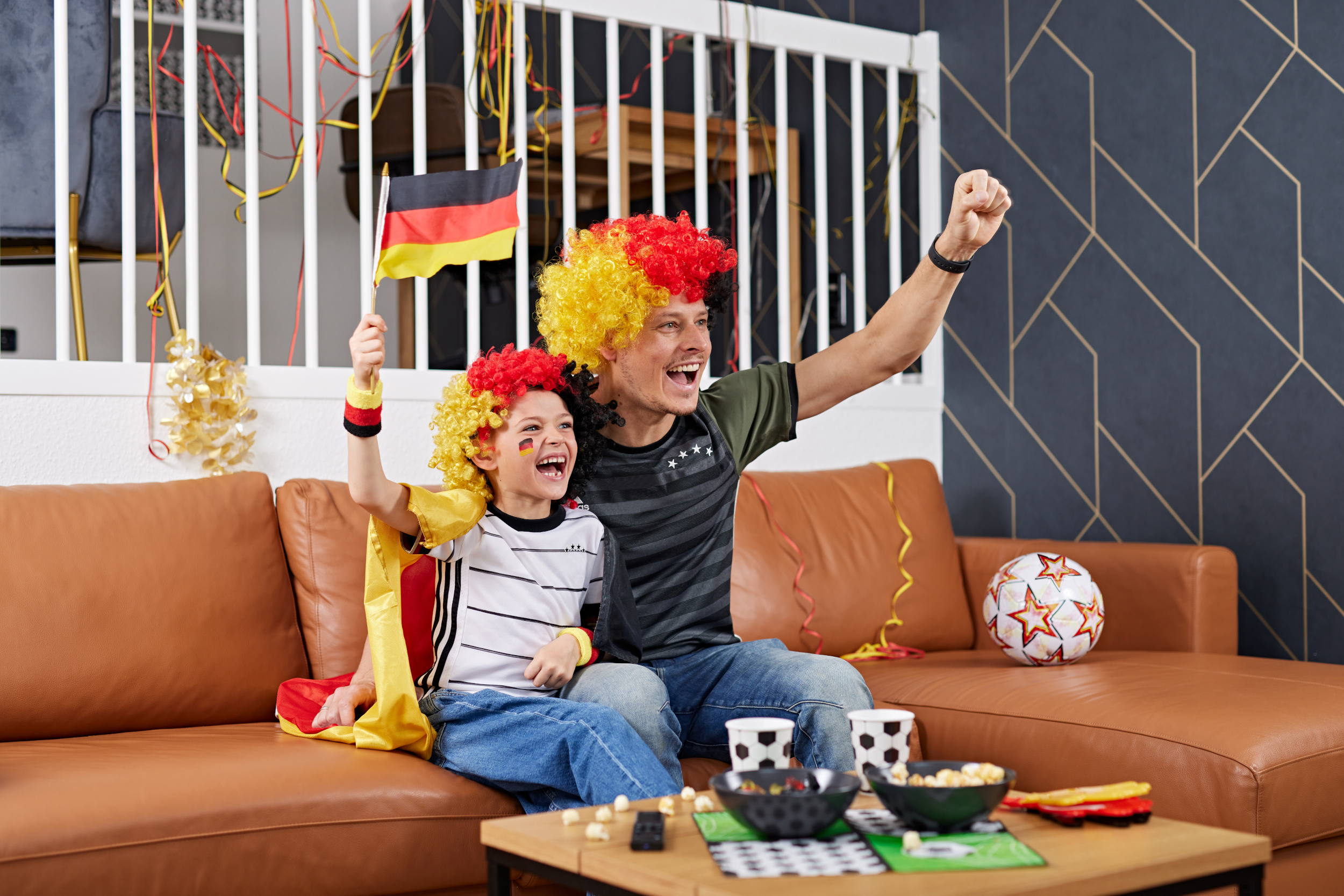 Vater und Sohn jubeln vorm Fernseher und tragen Deutschland Accessoires 