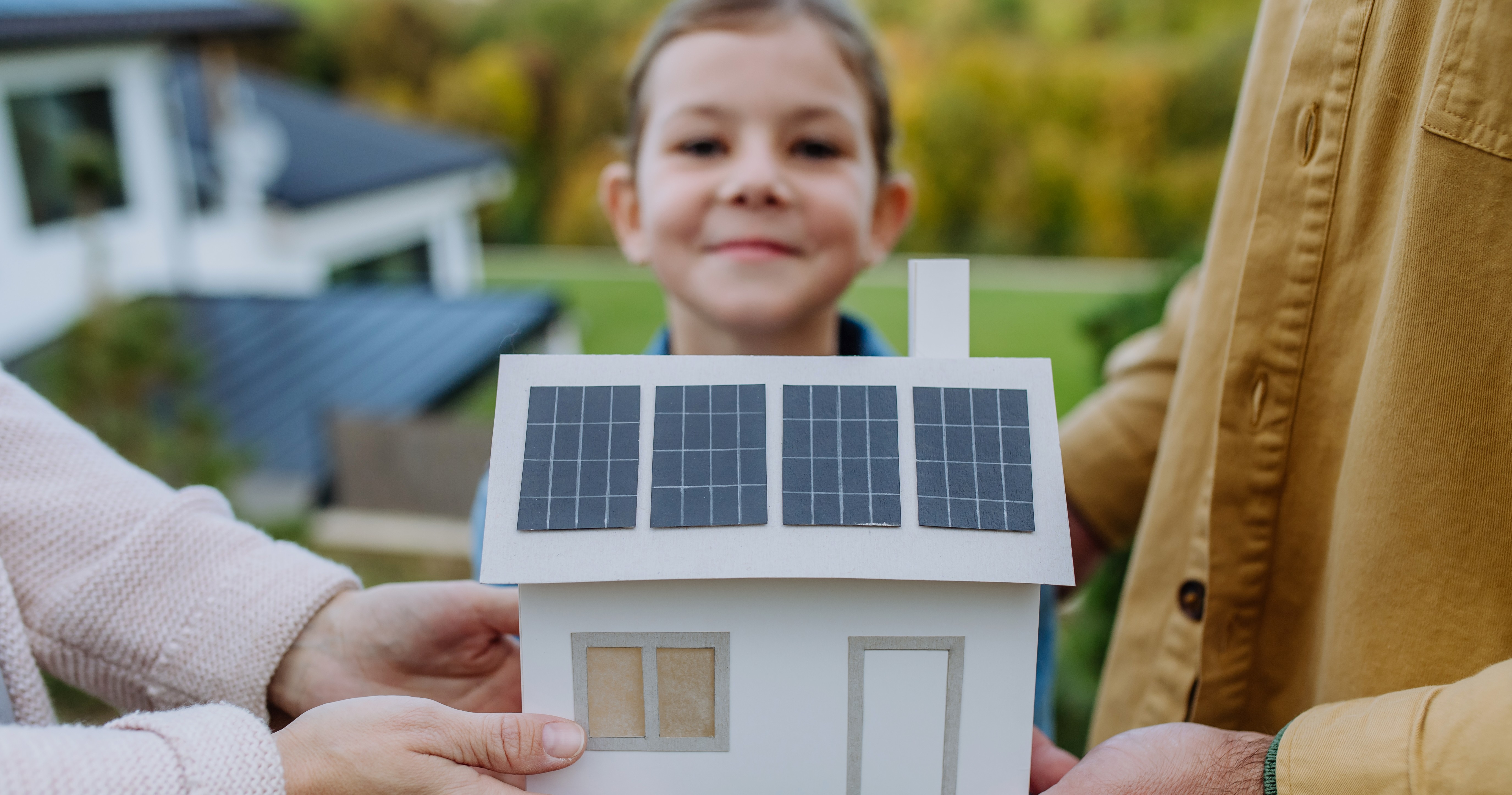 gebastelte Photovoltaikanlage auf einem Papierhaus mit Mädchen im Hintergrund